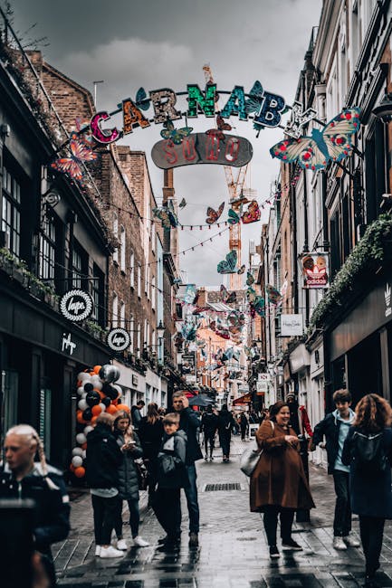 A street scene in Soho featuring an overhead sign with the word 'CARNABY' in large, colorful, letter-shaped lights, with the smaller sign below reading 'SUHO' in white letters on a grey background. Th