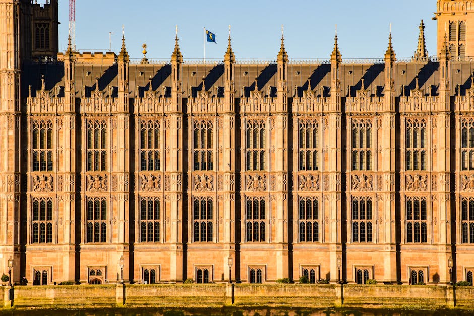 Close-up view of the detailed exterior facade of a historic Gothic-style building, featuring tall, pointed arched windows with intricate stone tracery, decorative carvings around the window frames, an